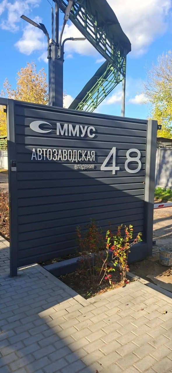 белые фрезерованные буквы ммyc и адрес автозаводская 48 на сером реечном заборе