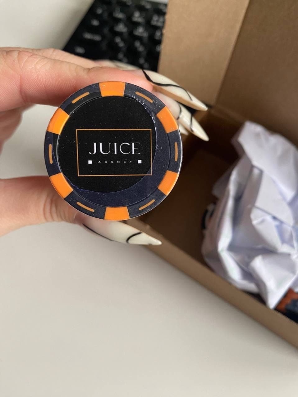 Черно-оранжевая брендированная покерная фишка с логотипом JUICE AGENCY в руке